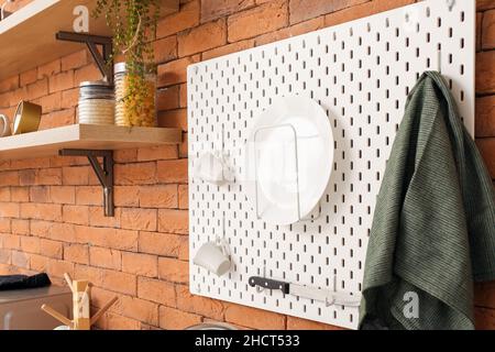 Peg board with kitchenware hanging on brick wall Stock Photo