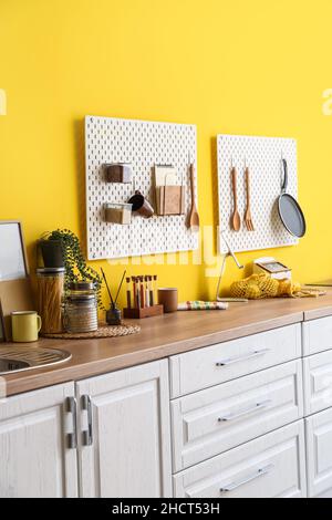 Peg boards with kitchenware hanging on yellow wall Stock Photo