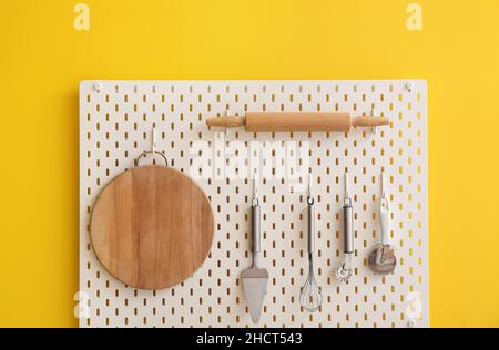 Peg board with kitchenware hanging on yellow wall Stock Photo
