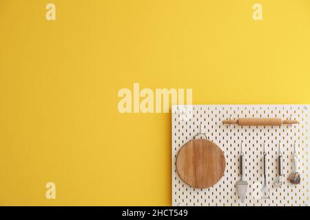 Peg board with kitchenware hanging on yellow wall Stock Photo