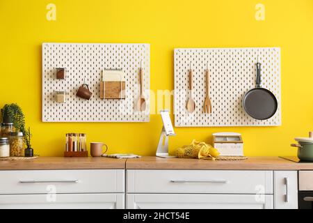 Peg boards with kitchenware hanging on yellow wall Stock Photo