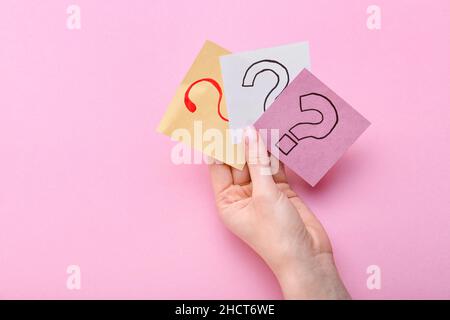 Woman holding sticky notes with question marks on pink background Stock Photo