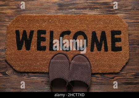 Door mat with word WELCOME and slippers on dark wooden floor Stock Photo