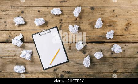 Clipboard with white sheet and pen with Crumpled paper balls on wood table background, copyspace for your individual text. Stock Photo