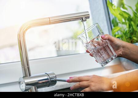 woman holding glass at water tap and filling water Stock Photo