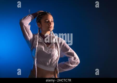 Urban session. Young caucasian woman with long white braids on a blue plain background, rap or trap dancer, alternative posing Stock Photo