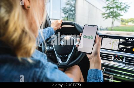 Woman hand holding iphone Xs with logo of Grab application in a car. Grab is smartphone app all-in-one transport booking in South-East Asia. Stock Photo