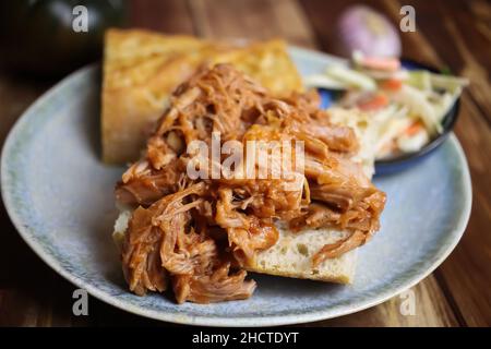 Closeup of dish with marinated pulled pork on fresh baguette, blurred cole slaw salad background Stock Photo