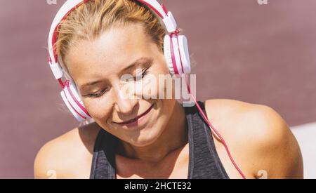 Young woman listening to music with earphones for fitness motivation. Portrait of a young woman in sportswear relaxing sitting getting inspired. Stock Photo