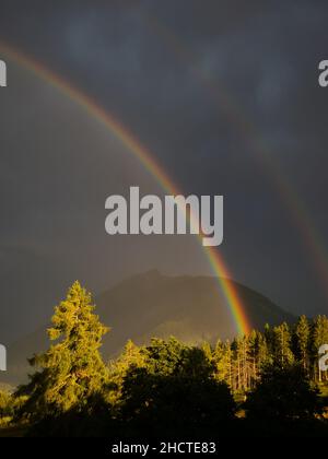 Rainbow on cloudy sky with mountain peaks in background. Summer landscape after storm. Stock Photo