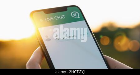 Person use customer service and support live chat with chatbot and automatic messages or human servant outdoor. Assistance and help with mobile phone Stock Photo