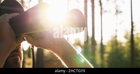 Beautiful Young Man Looking Through Binoculars At The forest On A Bright Sunny Day. Wanderlust Journey Concept Stock Photo