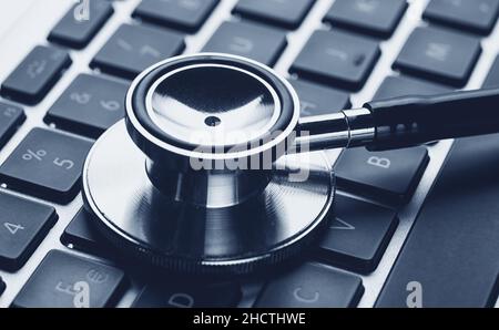 Silver stethoscope lying down on an laptop, blue toned Stock Photo