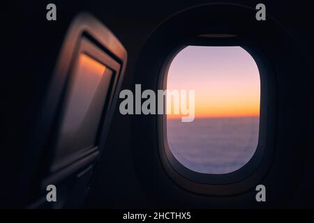 Window of airplane during flight above clouds at beautiful sunset. Stock Photo
