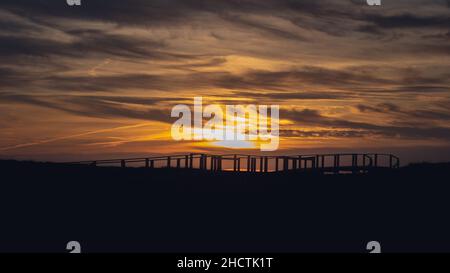 Dark golden sunset with dramatic cloudy sky over silhouette of boardwalk in Quiaios Beach, Portugal Stock Photo