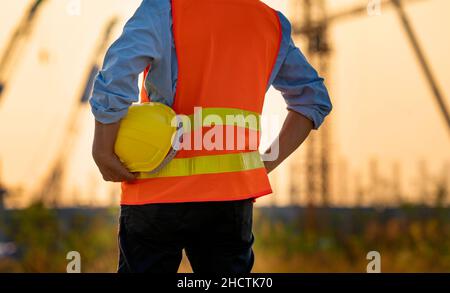 Man holding White helmet close up. Construction workers working on construction site.  Back side view Stock Photo