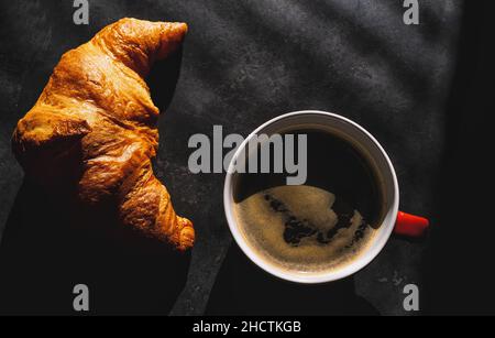 Croissants with coffee. french croissants on plate and red cup of coffee on a dark table background, top view Stock Photo