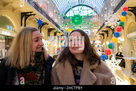 Two young beautiful female friends at the shopping mall smiling, admire the bright Christmas decor. Stock Photo