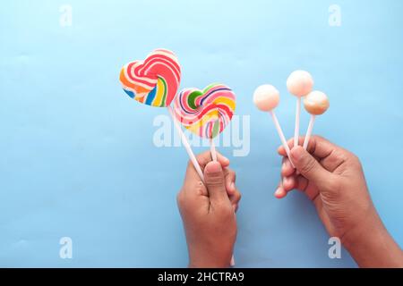 holding rainbow heart shape lollipop on blue background  Stock Photo