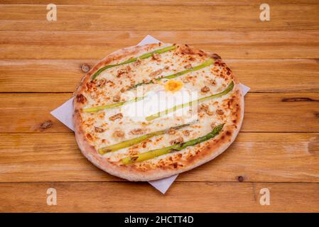 Pizza with wild asparagus, chopped walnuts and fried egg in the center with mozzarella cheese Stock Photo