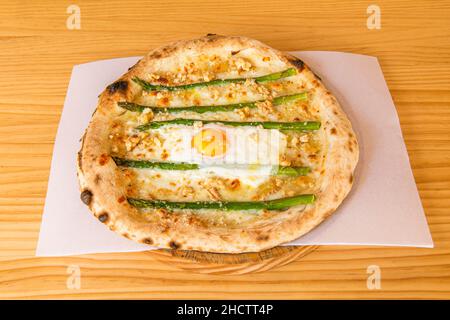 Pizza with wild asparagus, chopped walnuts and fried egg in the center with mozzarella cheese Stock Photo
