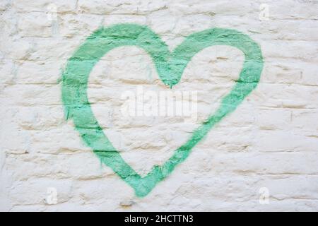 A green heart painted on a distressed white brick wall. Stock Photo