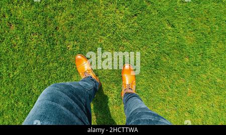 Young man standing in freshly mown grass lawn, top view of casually dressed person in leather shoes Stock Photo