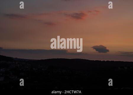 The partially cloudy sky turns red at sunset time over a village in the Galilee mountains, Israel. Stock Photo