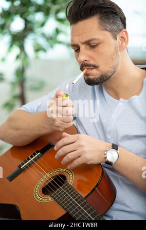 handsome man smoking a cigarette while holding an acoustic guitar Stock  Photo