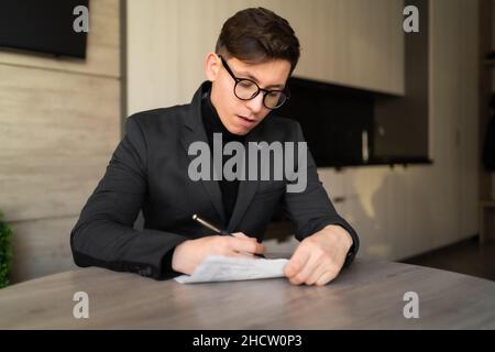 young man portrait, online webinar training coach, sitting at the table writing down ideas, paper work, businessman working at home Stock Photo