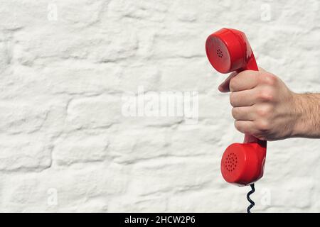 red handset in hand on a brick wall background Stock Photo