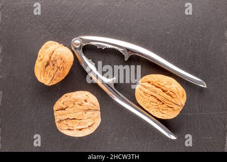 Three walnuts and a metal nutcracker on a slate stone, close-up, top view. Stock Photo