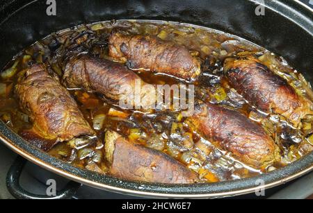 Closeup of isolated black metal casserole pot in oven with typical german fresh homemade beef roulades in sauce Stock Photo