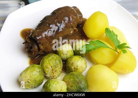 Closeup of isolated white plate with fresh homemade typical german beef roulades, brown sauce, cooked potatoes and green brussels sprouts Stock Photo