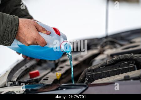 driver refilling the blue non-freezing windshield washer liquid in the tank of the car, closeup Stock Photo