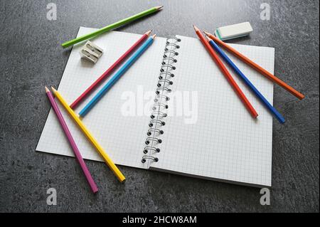 Desk for creative work with a blank open spiral notebook, crayons, sharpener and eraser on a dark gray table, copy space, selected focus, narrow depth Stock Photo