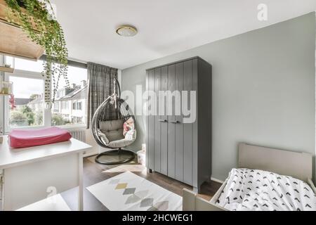 Stylish gray children's room with a wooden crib, a comfortable chair and a white table Stock Photo