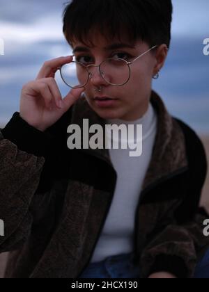 young trans woman taking off her glasses while looking intently at the camera Stock Photo
