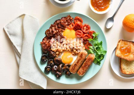 Full english breakfast with fried egg, bacon, sausage, beans and mushrooms on light background. Top view, flat lay Stock Photo