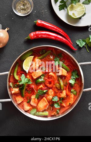 Thai style red chicken curry with vegetables in pan over black stone background. Top view, flat lay Stock Photo