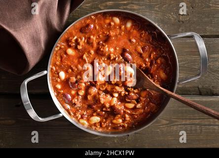 Stewed beans with ground beef, jalapeno pepper and bacon in cooking pan over wooden background. Top view, flat lay, close up Stock Photo