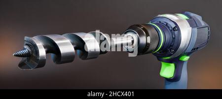 Close-up of auger bit in cordless drill on gray orange panoramic background. Metal drilling tool with cone thread center tip in power screw gun chuck. Stock Photo