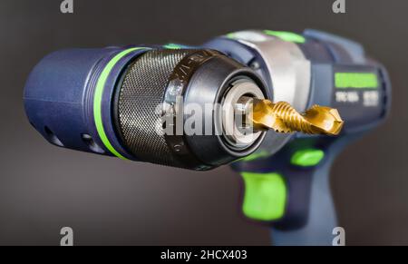 Steel tap and drill bit in power screwdriver right angle head on a gray background. Closeup of spiral fluted cutting tool in cordless drilling machine. Stock Photo
