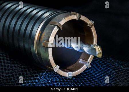 Hole saw cutter detail with spiral pilot drill bit on blue net with black background. Closeup a steel tip of sharp metal tool. Diamond inserts  crown. Stock Photo