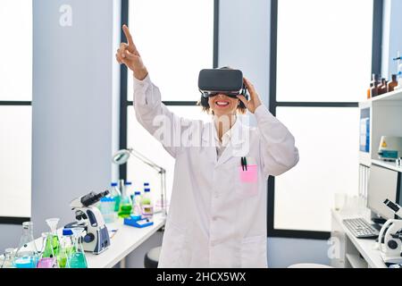 Young woman wearing scientist uniform using virtual reality goggles at laboratory Stock Photo