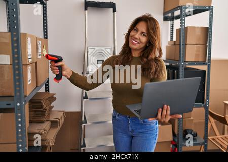 Young latin woman business worker scanning package using barcode reader at office Stock Photo