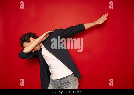 Happy man in casual making dab arms gesture on blank red studio background, funny white guy dabbing moving in internet meme pose celebrating victory having fun, dance school or triumph concept. High quality photo Stock Photo