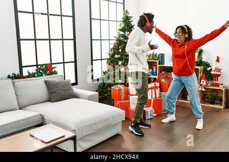 Young interracial couple smiling happy and and dancing standing by christmas tree at home. Stock Photo