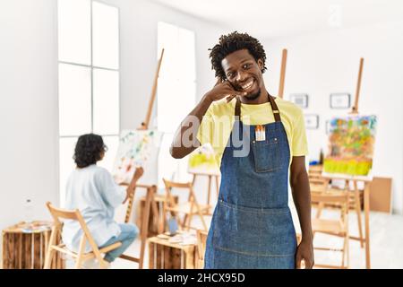 African young man standing at art studio smiling doing phone gesture with hand and fingers like talking on the telephone. communicating concepts. Stock Photo
