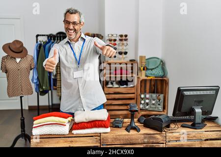 Middle age hispanic man working as manager at retail boutique approving doing positive gesture with hand, thumbs up smiling and happy for success. win Stock Photo